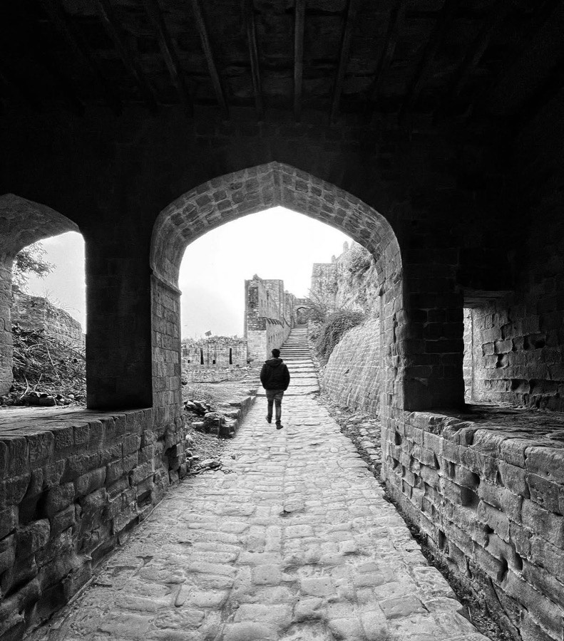 A stone archway at Kangra fort in black and white, a figure walking out towards the steps.